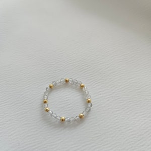 May include: A delicate bracelet made of clear and iridescent beads with gold accents. The bracelet is made of small, round beads that are strung together on a thin, flexible cord.