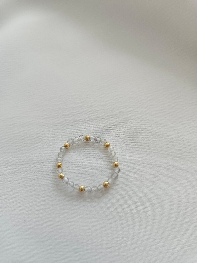 May include: A delicate bracelet made of clear and iridescent beads with gold accents. The bracelet is made of small, round beads that are strung together on a thin, flexible cord.