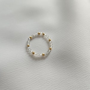 May include: A delicate ring made of clear beads and gold accents. The ring is simple and elegant, perfect for everyday wear.