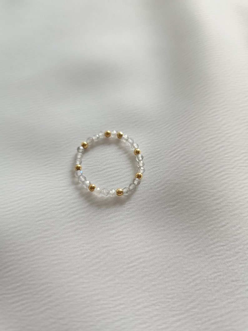 May include: A delicate ring made of clear beads and gold accents. The ring is simple and elegant, perfect for everyday wear.
