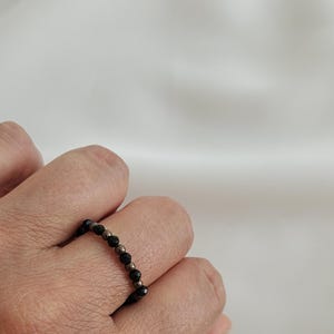 K&ouml;nnte beinhalten: Ein schwarzer und silberner Perlenring, der an einem Finger getragen wird.