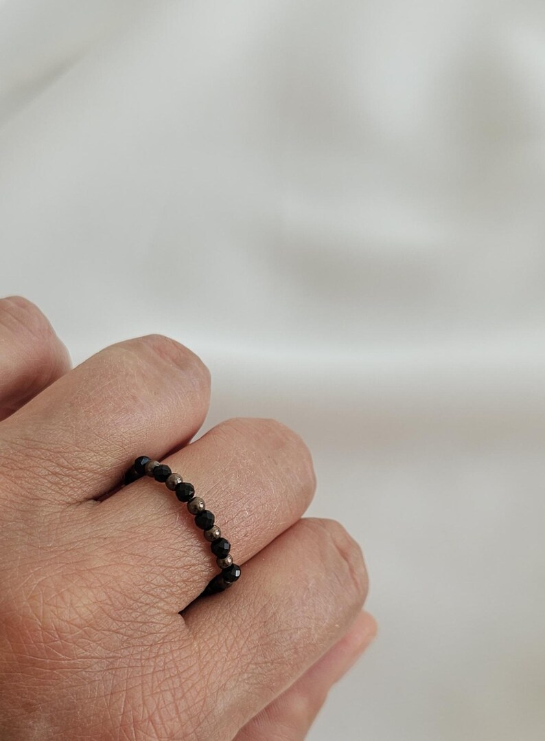 K&ouml;nnte beinhalten: Ein schwarzer und silberner Perlenring, der an einem Finger getragen wird.