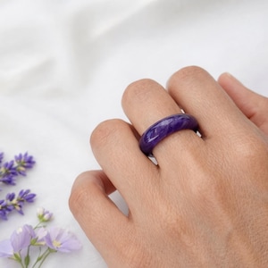 Può includere: Un anello di colore viola intenso, liscio e lucido, con un profilo a fascia arrotondato. L'anello presenta un colore solido e uniforme su tutta la superficie, con una finitura lucida che riflette la luce. La fascia è circolare e regolare.