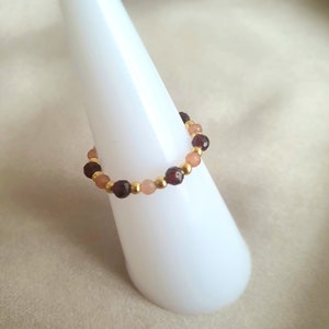 May include: A gold ring with red, pink, and gold beads. The ring is on a white display stand.