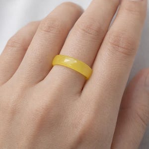 Puede incluir: Un anillo de banda amarillo sólido y liso con un acabado pulido. El anillo presenta un diseño circular simple y continuo con un ancho uniforme y un perfil redondeado, mostrando un color amarillo brillante y vibrante en toda la pieza.