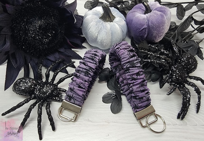 Purple cotton fabric with black spiders design. The keychain uses 7.5 inch to 8 inch wide elastic to make it stretchy. The keychain is completed with silver colored key fob clamps and silver keyring.