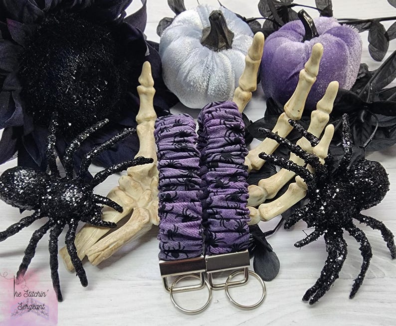 Purple cotton fabric with black spiders design. The keychain uses 7.5 inch to 8 inch wide elastic to make it stretchy. The keychain is completed with silver colored key fob clamps and silver keyring.