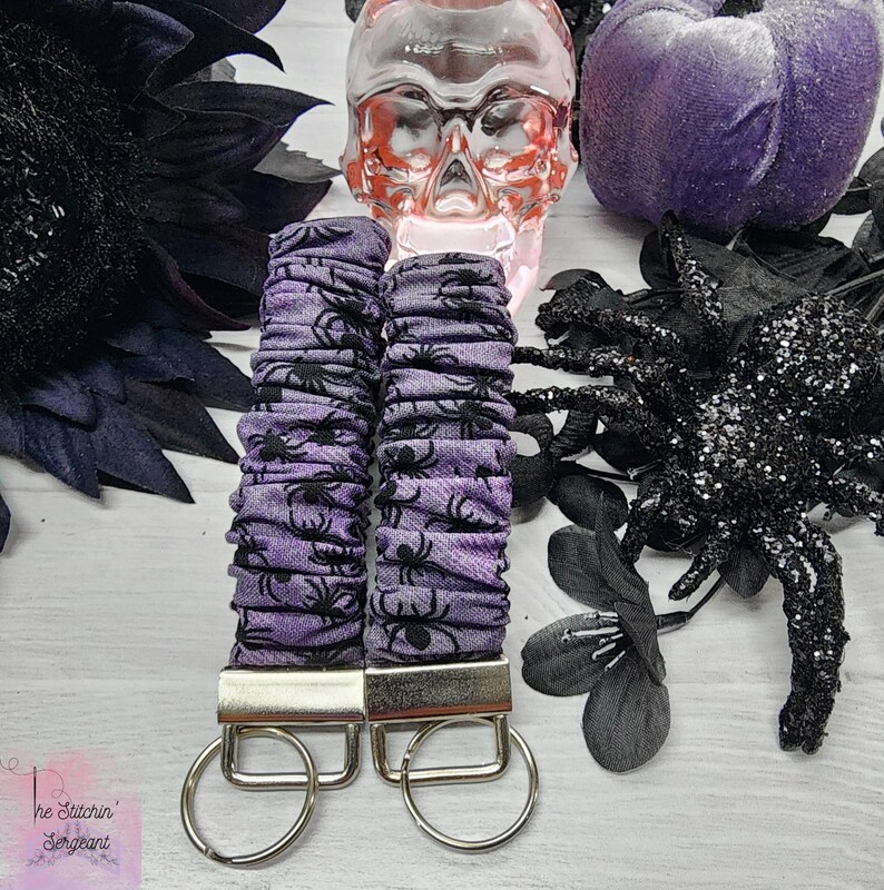 Purple cotton fabric with black spiders design. The keychain uses 7.5 inch to 8 inch wide elastic to make it stretchy. The keychain is completed with silver colored key fob clamps and silver keyring.