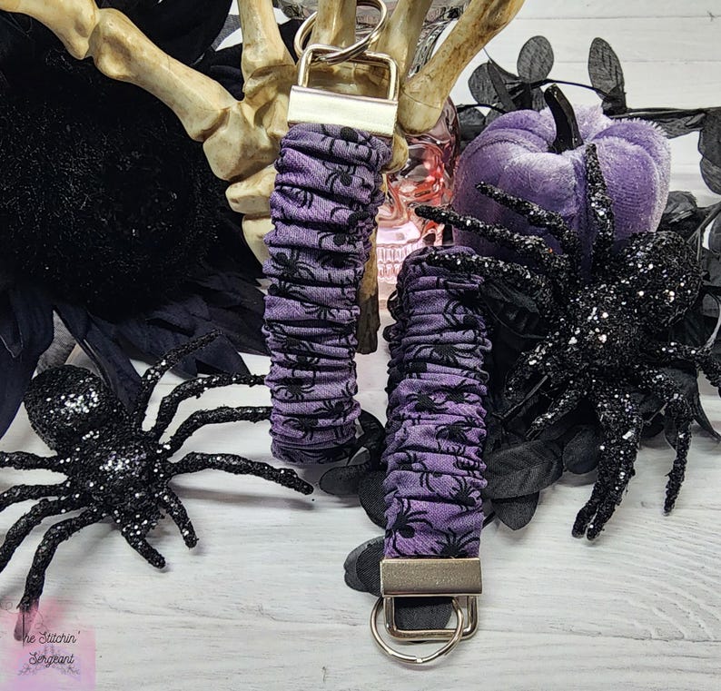 Purple cotton fabric with black spiders design. The keychain uses 7.5 inch to 8 inch wide elastic to make it stretchy. The keychain is completed with silver colored key fob clamps and silver keyring.