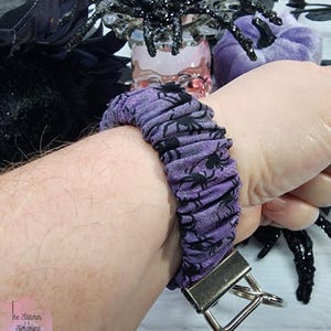 Purple cotton fabric with black spiders design. The keychain uses 7.5 inch to 8 inch wide elastic to make it stretchy. The keychain is completed with silver colored key fob clamps and silver keyring.