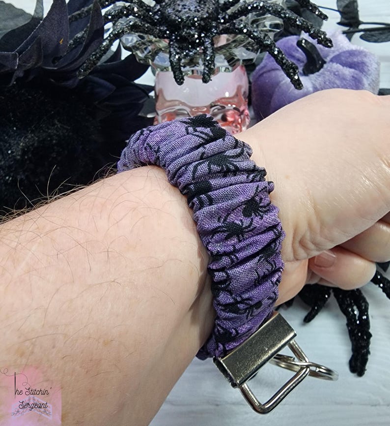 Purple cotton fabric with black spiders design. The keychain uses 7.5 inch to 8 inch wide elastic to make it stretchy. The keychain is completed with silver colored key fob clamps and silver keyring.
