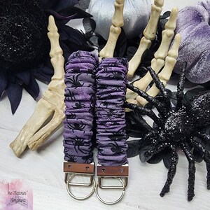 Purple cotton fabric with black spiders design. The keychain uses 7.5 inch to 8 inch wide elastic to make it stretchy. The keychain is completed with silver colored key fob clamps and silver keyring.