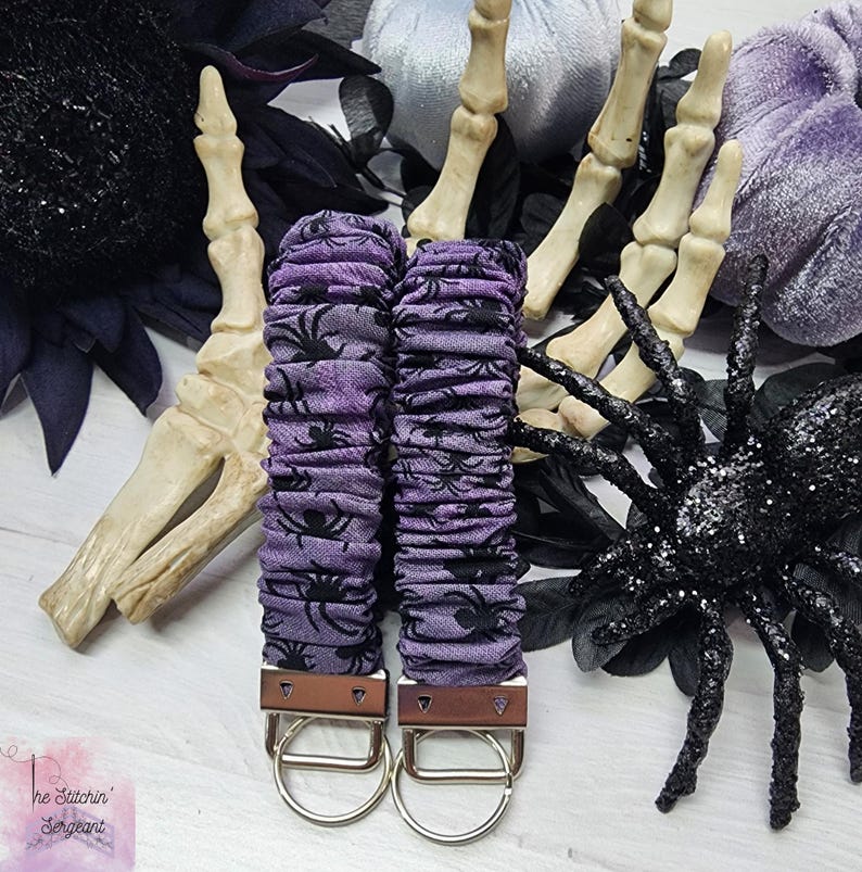 Purple cotton fabric with black spiders design. The keychain uses 7.5 inch to 8 inch wide elastic to make it stretchy. The keychain is completed with silver colored key fob clamps and silver keyring.