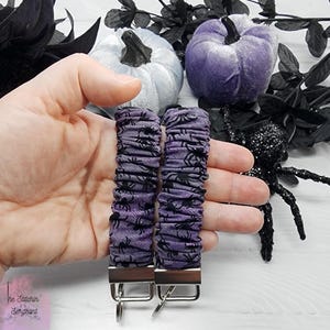 Purple cotton fabric with black spiders design. The keychain uses 7.5 inch to 8 inch wide elastic to make it stretchy. The keychain is completed with silver colored key fob clamps and silver keyring.