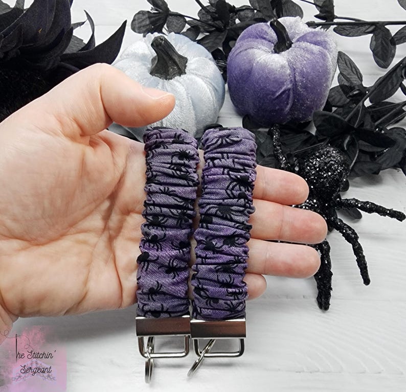 Purple cotton fabric with black spiders design. The keychain uses 7.5 inch to 8 inch wide elastic to make it stretchy. The keychain is completed with silver colored key fob clamps and silver keyring.