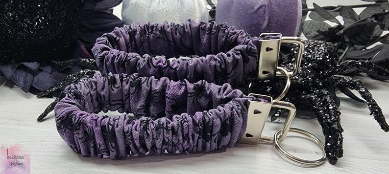 Purple cotton fabric with black spiders design. The keychain uses 7.5 inch to 8 inch wide elastic to make it stretchy. The keychain is completed with silver colored key fob clamps and silver keyring.