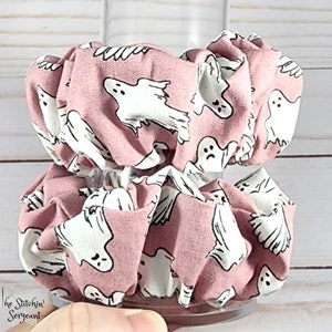 May include: Two pink fabric scrunchies with a white ghost pattern. The scrunchies are stacked on top of each other.