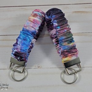 May include: A galaxy print fabric key chain with silver key rings. The fabric is a soft, stretchy material with a galaxy print in shades of blue, purple, pink, and white.