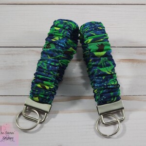 May include: Two green and blue patterned fabric keychains with silver key rings. The fabric is gathered and has a slightly textured look.