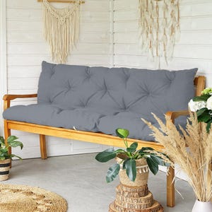Può includere: Un cuscino per panca grigio trapuntato su una panca in legno. Il cuscino è rettangolare e presenta un design trapuntato con bottoni. La panca è circondata da piante in cesti intrecciati e arazzi decorativi. Misura circa 150 cm di lunghezza.