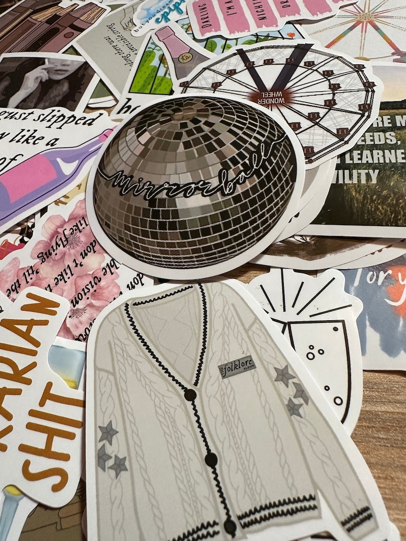 May include: A collection of stickers featuring various designs. Notable stickers include a disco ball with "mirrorball" script, a cable-knit cardigan with "folklore" text, and a Ferris wheel. Other stickers have text and illustrations.
