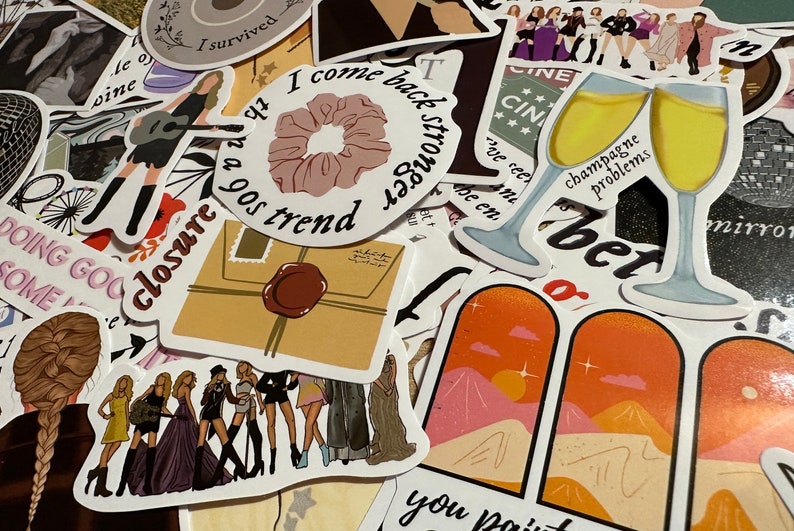 May include: A collection of colorful stickers with various designs and text. Some stickers feature illustrations of a woman playing guitar, a scrunchie, champagne glasses, and a group of women. Other stickers have phrases like "I come back stronger" and "champagne problems."