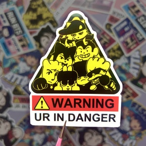May include: A yellow and black warning sign sticker with a cartoon illustration of five characters. The sign reads "WARNING UR IN DANGER".