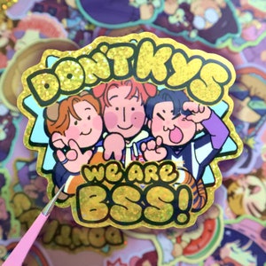 May include: A gold glitter sticker with three cartoon characters and the text "Don't Kiss Us We Are Boss!"