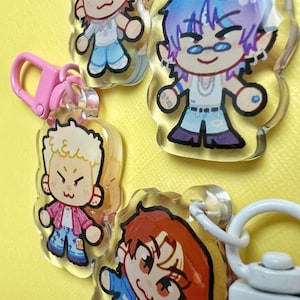 May include: A collection of clear acrylic keychains featuring cartoon character illustrations. The keychains have pink and white hardware. The characters have various hair colors and wear different outfits. The background is a solid yellow.