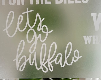 May include: White frosted glass sign with the text "Let's go Buffalo" in cursive script and "What" in block letters.