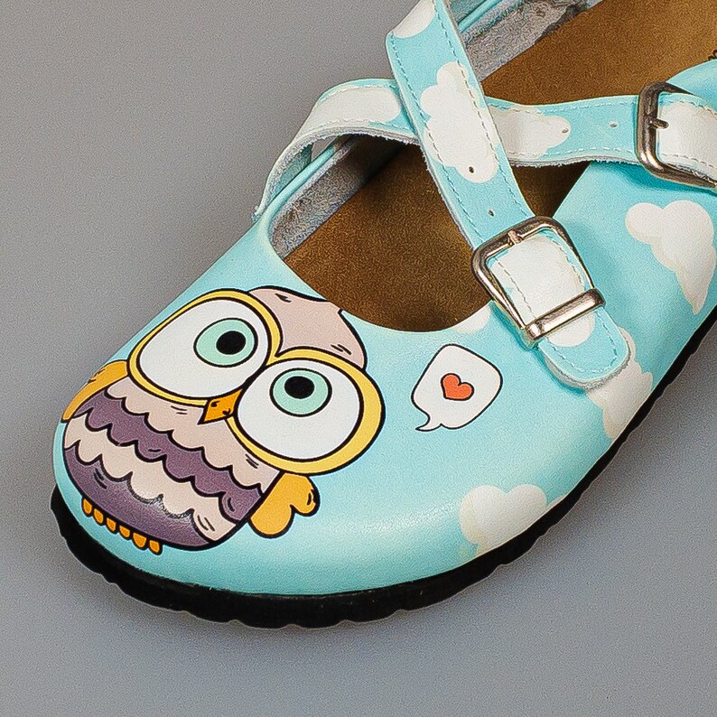 May include: Light blue children's shoes with a white strap and buckle. The shoes feature a cartoon owl with big eyes and a heart-shaped speech bubble.