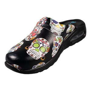 May include: Black slip-on clogs with a colorful sugar skull pattern. The clogs have a thick, black sole with a white trim.