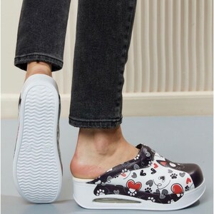 Op de afbeelding: Witte en zwarte slip-on klomp met een zwarte kat en rode hart print. De klomp heeft een witte platformzool.