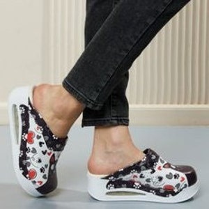 Op de afbeelding: Witte en zwarte platform slippers met een rood hart en pootprint ontwerp.