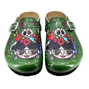 May include: A pair of green clogs featuring a colourful illustration of a woman with a flower crown and a skull. The clogs have a buckle strap and a white polka dot pattern.