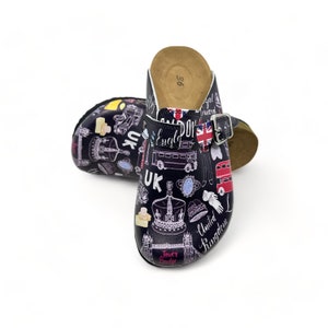 May include: A pair of black and white clogs with a London theme. The clogs feature images of the London Eye, Big Ben, a double-decker bus, and the Union Jack flag. The text "United Kingdom" is printed on the clogs.