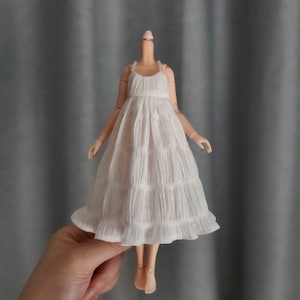 May include: A white, tiered, sleeveless dress with a ruffled hem. The dress is made of a lightweight fabric and has a simple, elegant design.