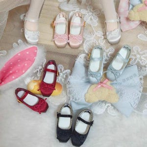 Könnte beinhalten: Eine Sammlung von Miniatur-Mary-Jane-Schuhen für Puppen in verschiedenen Farben wie Weiß, Rosa, Rot, Hellblau und Schwarz. Jedes Paar hat eine abgerundete Zehenpartie, einen dünnen Riemen mit einer kleinen Schnalle und eine dekorative Schleife.