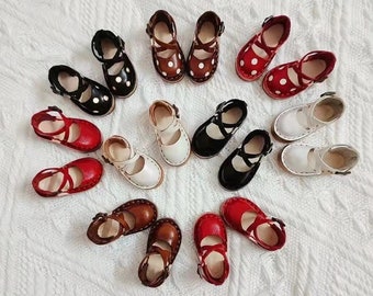 Könnte beinhalten: Eine Sammlung von 15 Paaren Miniaturschuhen in verschiedenen Farben, darunter Rot, Weiß, Schwarz und Braun. Die Schuhe haben ein schlichtes Design mit einem Riemen über dem Oberteil und einem Schnallenverschluss. Einige der Schuhe haben weiße Punkte.