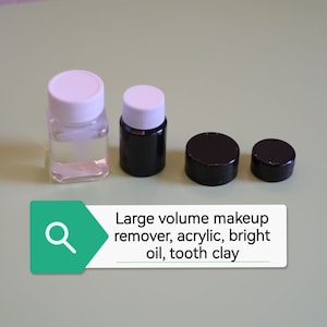 Peut inclure: Quatre petits contenants, deux en verre transparent avec des couvercles blancs et deux en plastique noir avec des couvercles noirs. Les contenants sont disposés en rangée sur une surface vert clair. Le texte "Large volume makeup remover, acrylic, bright oil, tooth clay" est visible sur l'image.