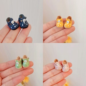 May include: Four pairs of miniature doll shoes with white polka dots. The shoes are in four different colors: navy blue, yellow, green, and pink.