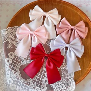 Peut inclure: Un ensemble de cinq nœuds en ruban satiné dans des tons blanc, rose clair, vieux rose et rouge profond. Chaque nœud présente un design classique à plusieurs boucles avec deux longs pans tombants, fabriqué dans un tissu lisse et brillant.