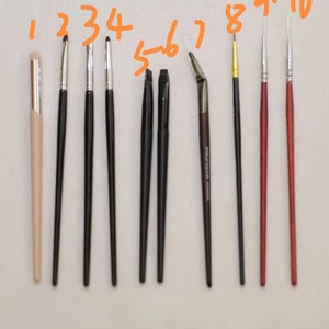 May include: Ten different makeup brushes with numbered labels. The brushes are arranged in a row from left to right. The brushes are all different sizes and shapes. The brushes are all made of different materials, including natural and synthetic bristles.