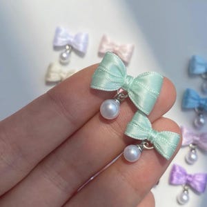 Peut inclure: Gros plan sur plusieurs nœuds en ruban de couleur pastel avec des fausses perles pendantes. Les nœuds sont dans des tons de vert menthe, bleu clair, rose, violet et blanc. Les nœuds sont petits et délicats, avec une finition brillante. Les perles sont rondes et blanches.