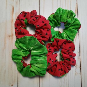 May include: Three red and green fabric scrunchies with a watermelon print. The scrunchies are made of soft, stretchy fabric and are perfect for holding hair in place.