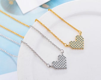 May include: Two delicate necklaces with heart-shaped pendants. One necklace is silver-toned, the other is gold-toned. The heart pendants are covered in small, sparkling stones. The necklaces are displayed on a white surface.