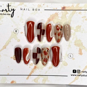 Op de afbeelding: Een set van tien kunstnagels met verschillende ontwerpen. De nagels zijn in twee rijen gerangschikt, gelabeld met "R" en "L" voor de rechter- en linkerhand. De ontwerpen omvatten abstracte swirls, geometrische vormen en een bloemenpatroon. De nagels zijn een mix van bruin, wit en goud.