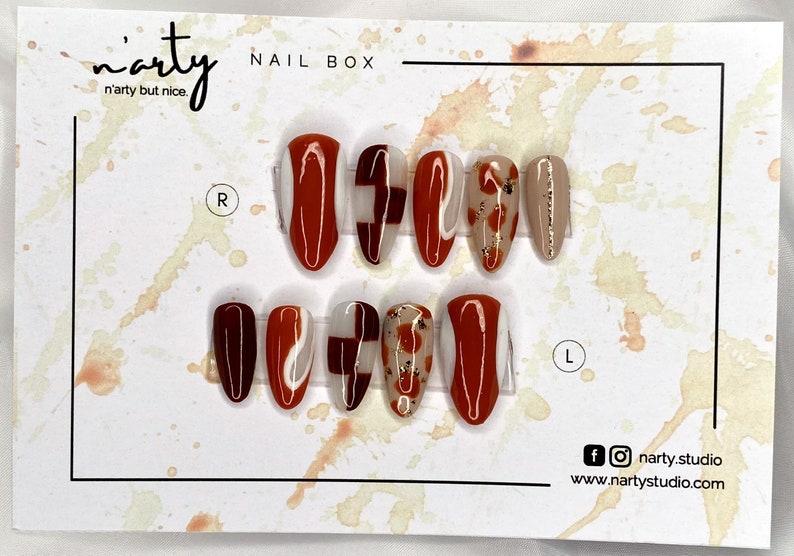 Op de afbeelding: Een set van tien kunstnagels met verschillende ontwerpen. De nagels zijn in twee rijen gerangschikt, gelabeld met "R" en "L" voor de rechter- en linkerhand. De ontwerpen omvatten abstracte swirls, geometrische vormen en een bloemenpatroon. De nagels zijn een mix van bruin, wit en goud.
