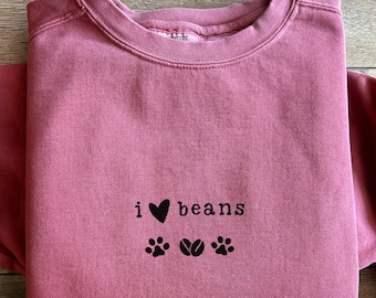 Puede incluir: Sudadera de color rojo carmesí con el texto "i ♥ beans" y huellas de patas y gráficos de granos de café.