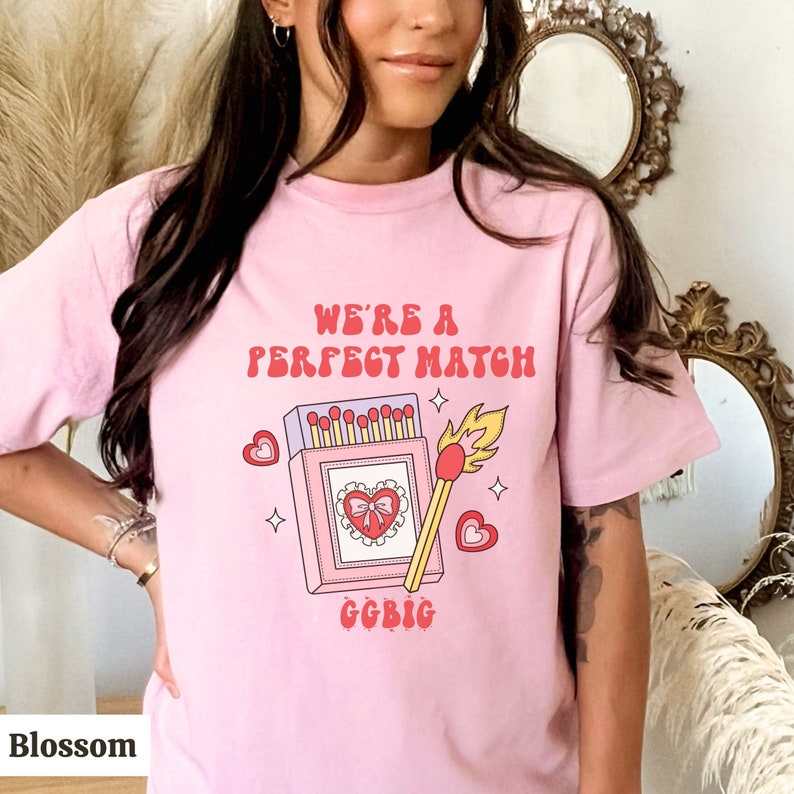 May include: Pink t-shirt with a graphic of a matchbox with a heart and the text "We're a Perfect Match" and "GGBIG" printed on it.